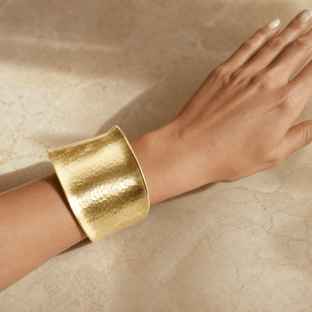 Photorealistic jewelry try-on: a wide hammered gold cuff bracelet on a model's wrist resting against a warm marble surfa