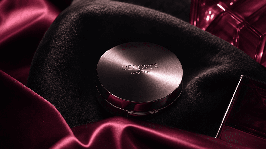 Layers of black wool, burgundy satin, brushed metal, and translucent cosmetic glass forming an atmospheric product stage