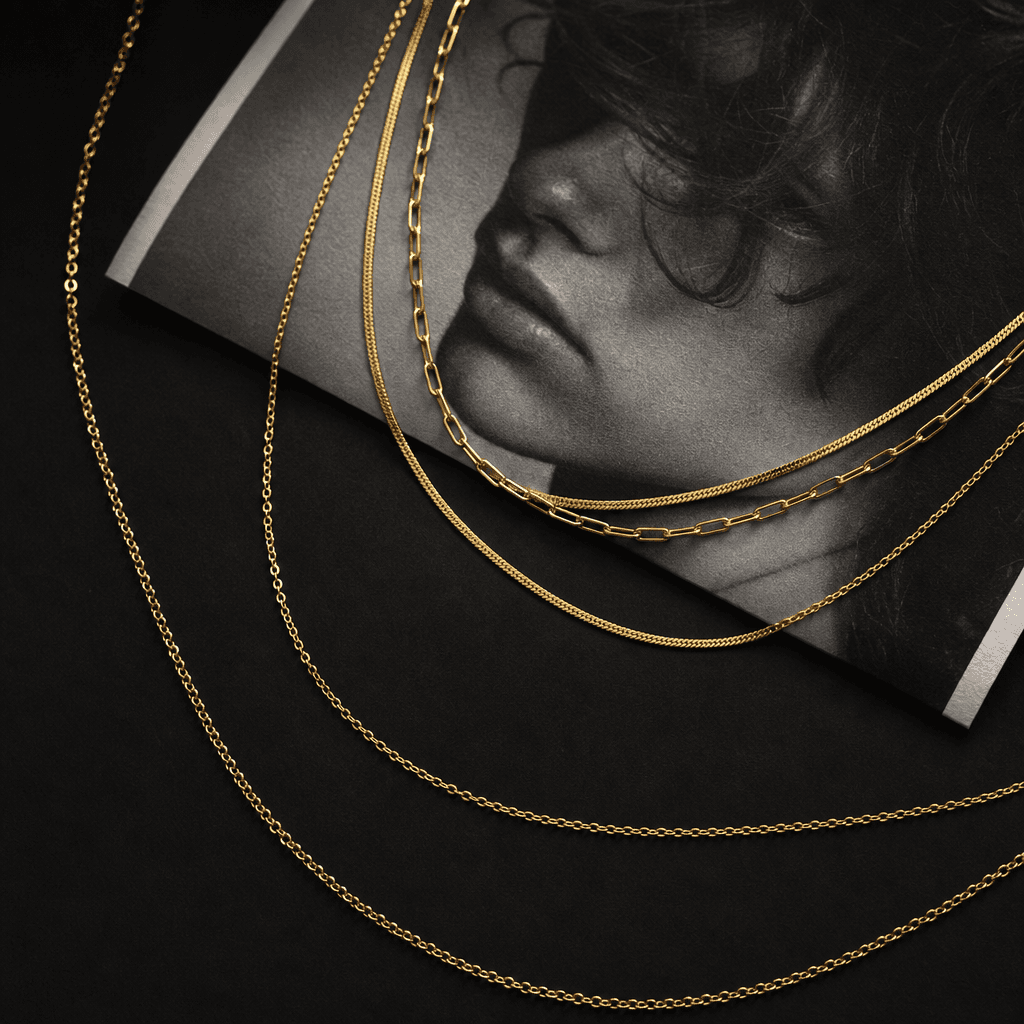 A layered fine gold chain necklace draped loosely across a folded black-and-white photographic print with visible grain 