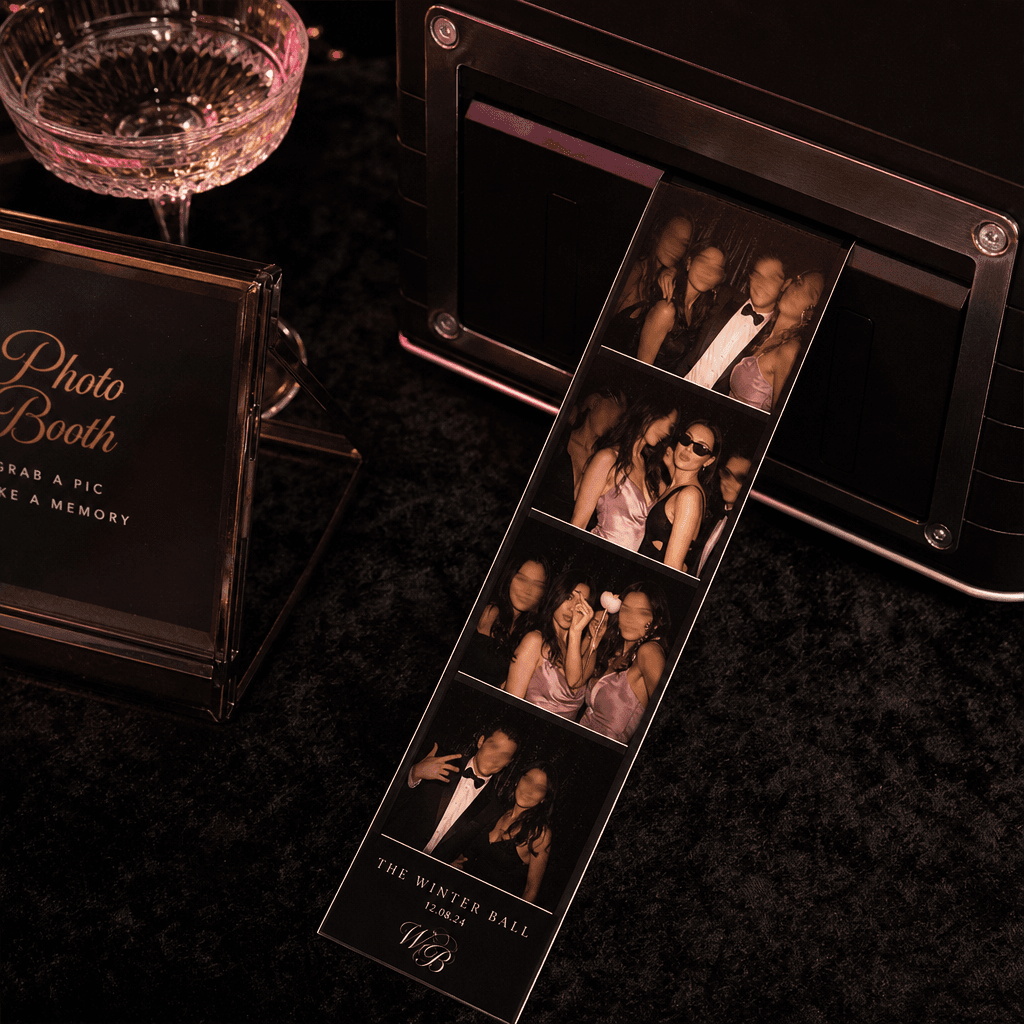 A square luxury event scene with freshly printed photobooth strips emerging onto a dark velvet table, each frame showing