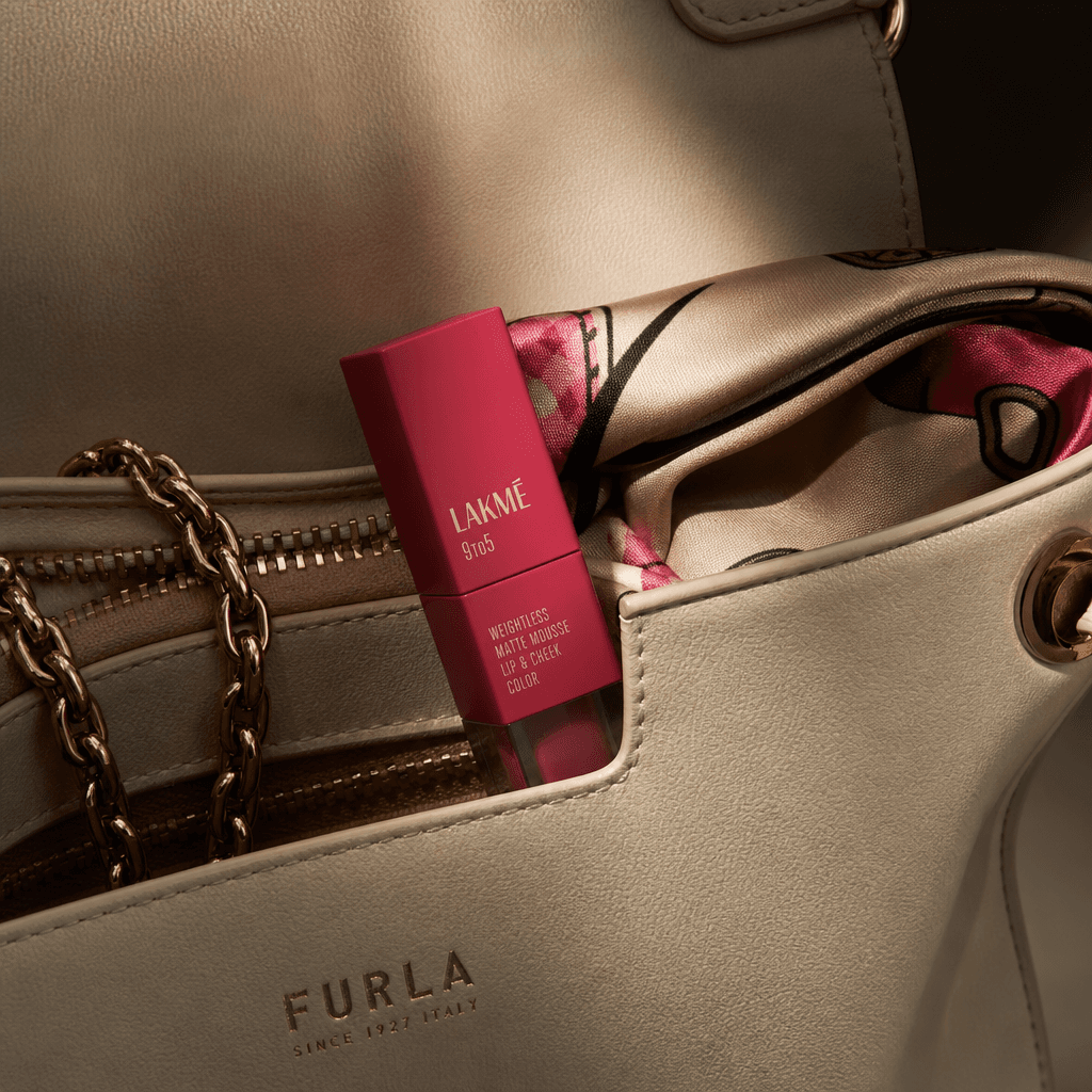 A compact matte lipstick resting inside the pocket of a cream leather handbag, partially revealed beside a fine chain an