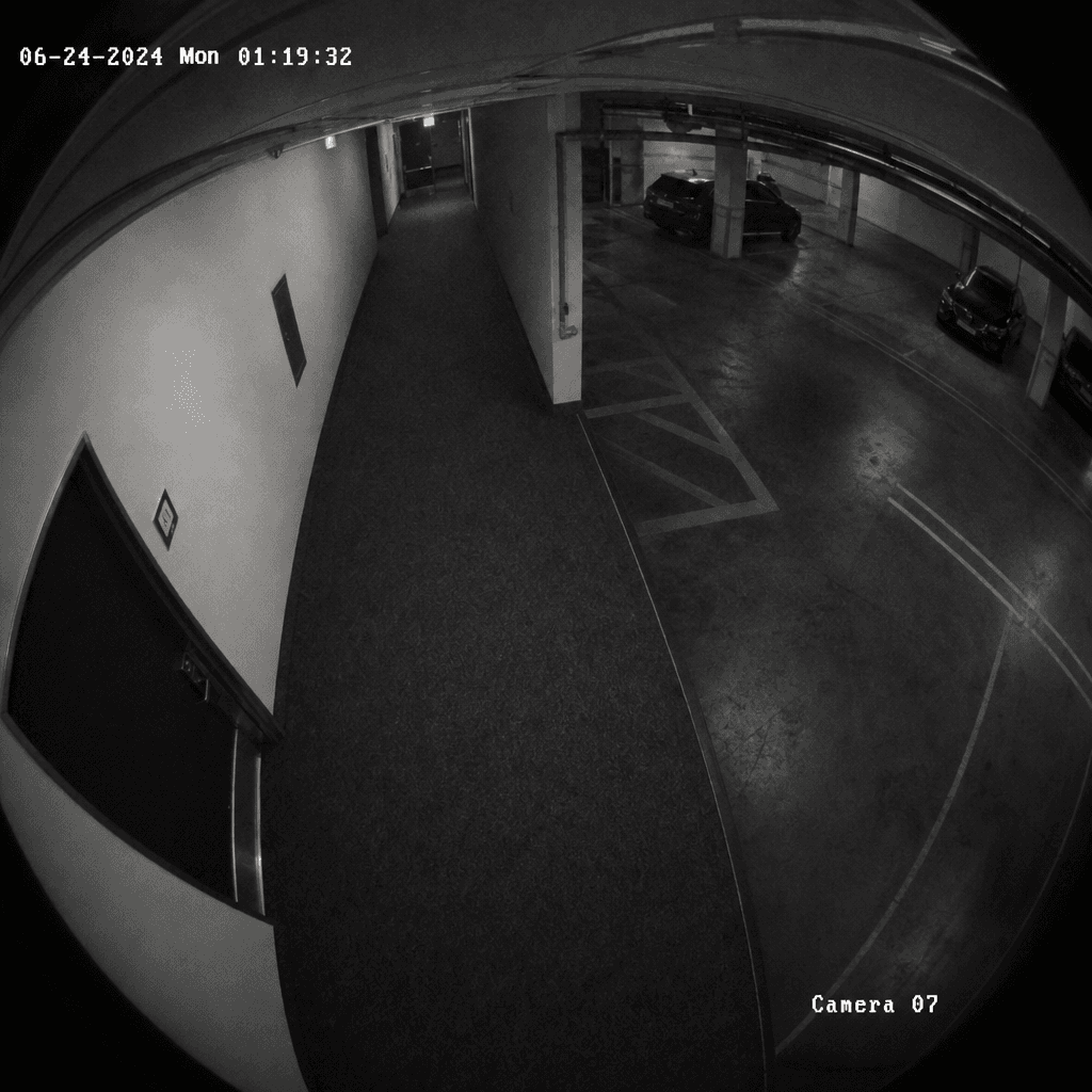 Fish-eye security camera lens effect with timestamp visible in corner, dark indoor space (parking garage interior or off