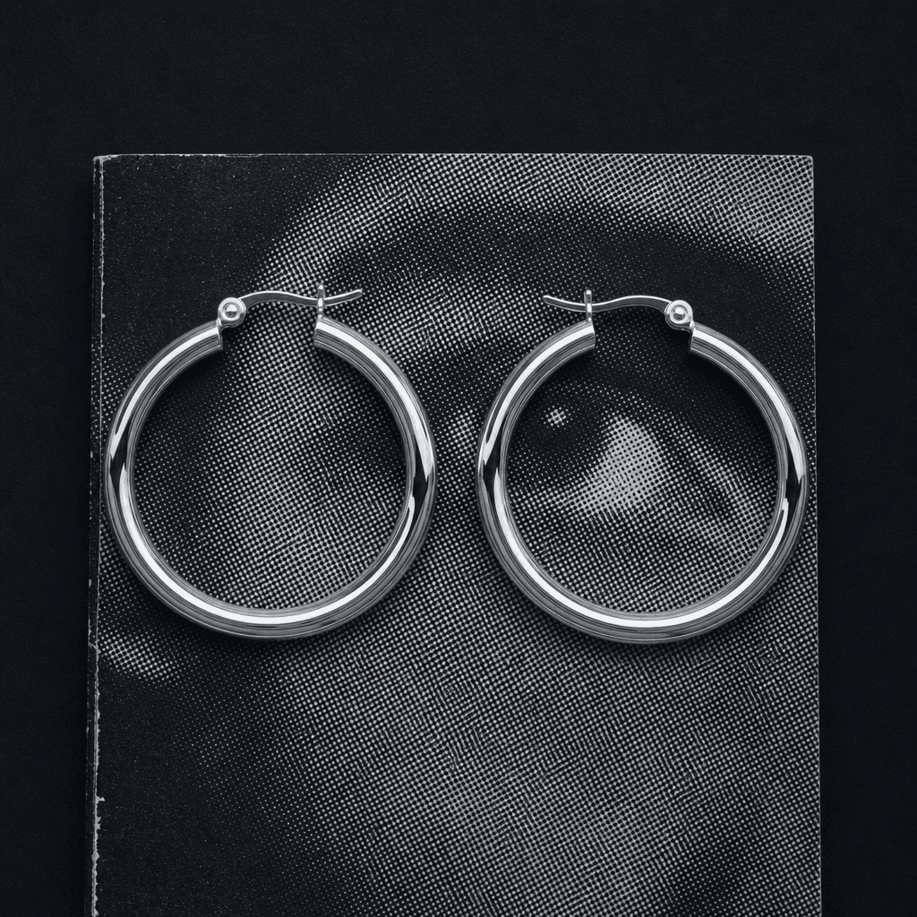 A pair of large silver hoop earrings arranged symmetrically on a textured black-and-white print with visible halftone do