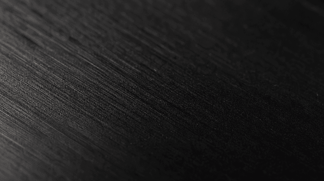 Extreme close-up macro of a premium textured material surface — brushed dark metal or matte ceramic — under precision st