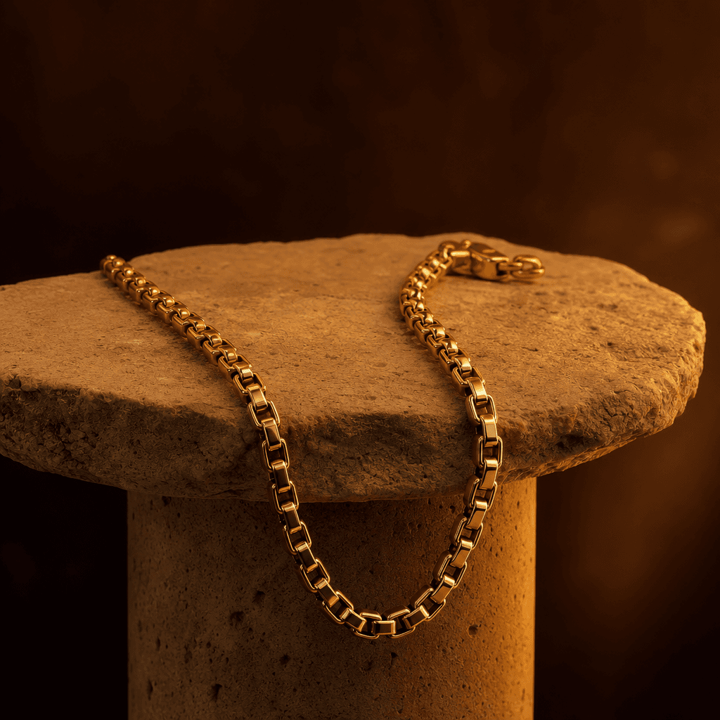 Gold chain necklace draped on stone pedestal with warm amber studio lighting, dark moody background, professional jewelr