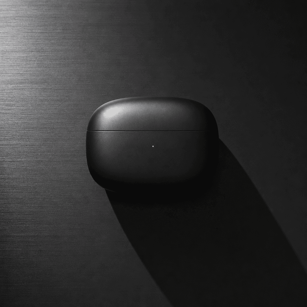 A sleek wireless earbud case photographed flat-lay on brushed anthracite surface. Single overhead key light creates hard