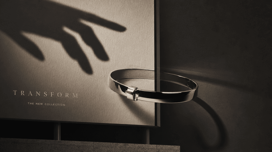 An abstract hand-shaped shadow reaches across a billboard surface as a polished bracelet crosses from printed paper into