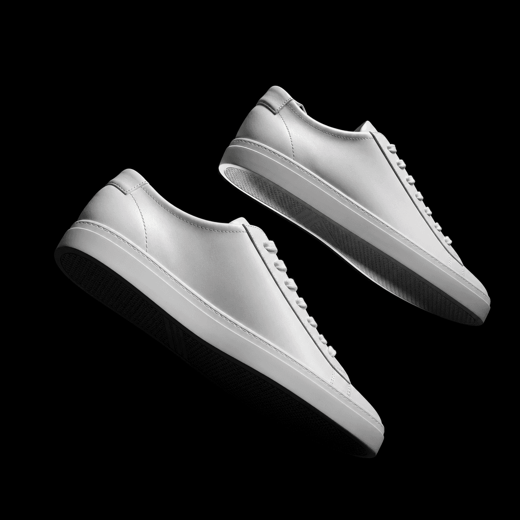 High-fashion footwear editorial: a pair of minimalist white leather sneakers floating at a slight angle against a pure b