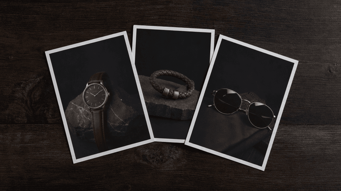 Minimalist editorial arrangement of three small product prints on matte paper fanned slightly on a dark wooden surface, 
