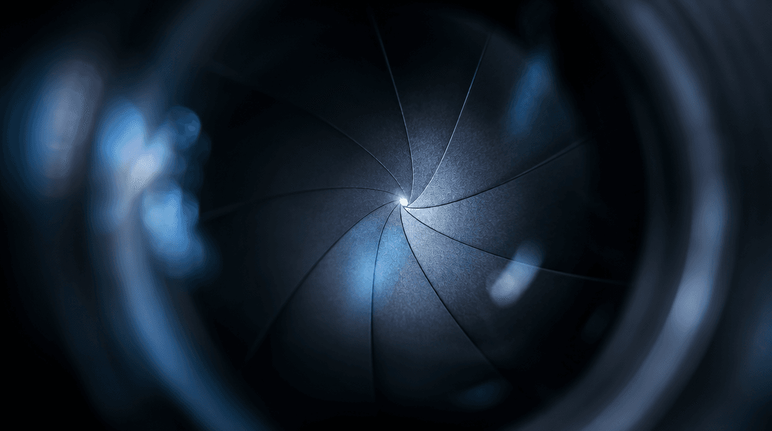 Abstract macro photograph of camera lens aperture blades open to a single sharp focal point, radiating soft bokeh haze o