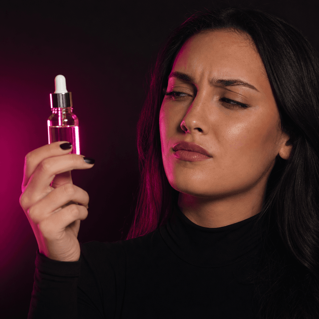 An anonymous beauty creator holding a premium serum bottle with a skeptical yet composed reaction, dark editorial studio