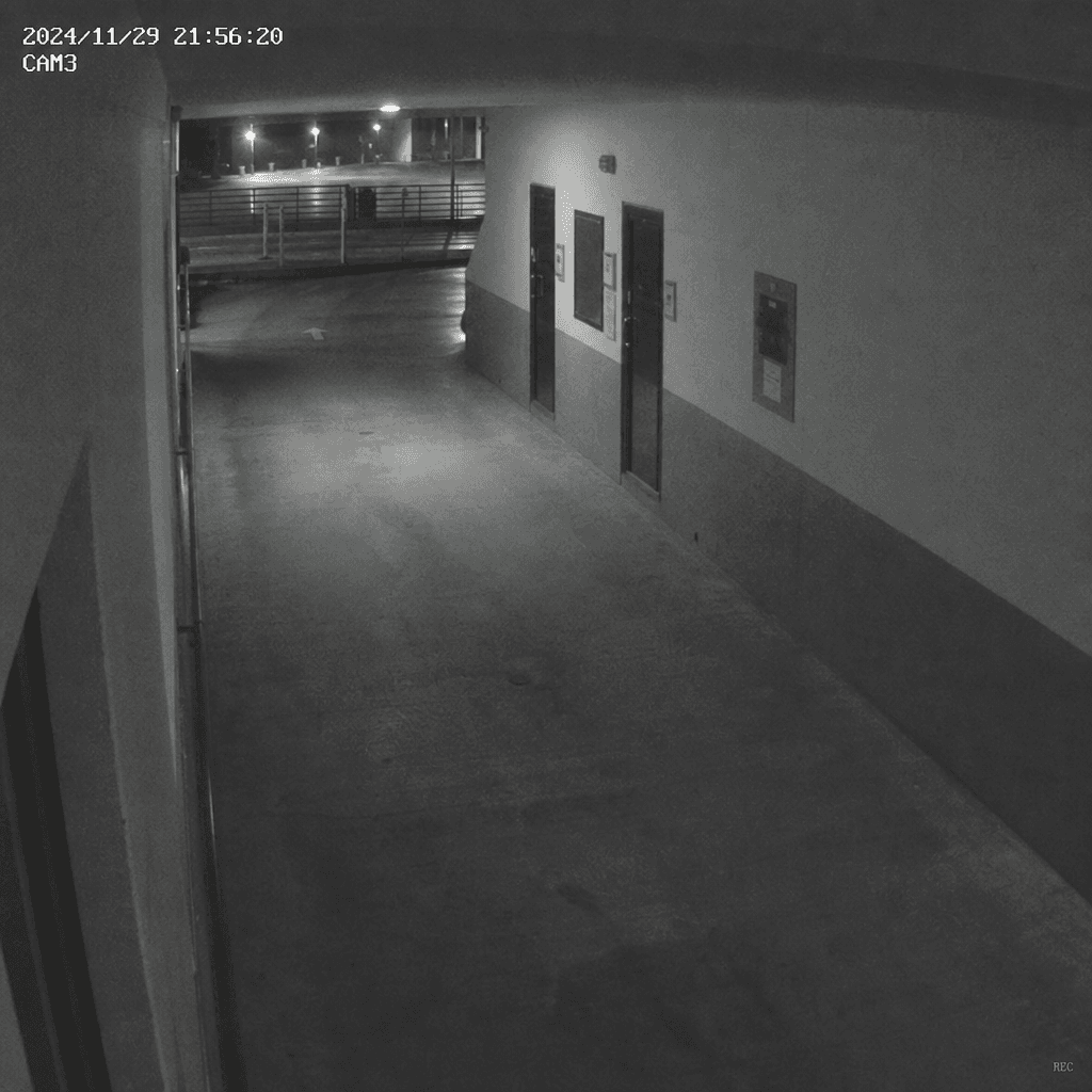 Wide security camera perspective of empty hallway or parking lot, grainy CCTV quality, glowing timestamp in corner, auth