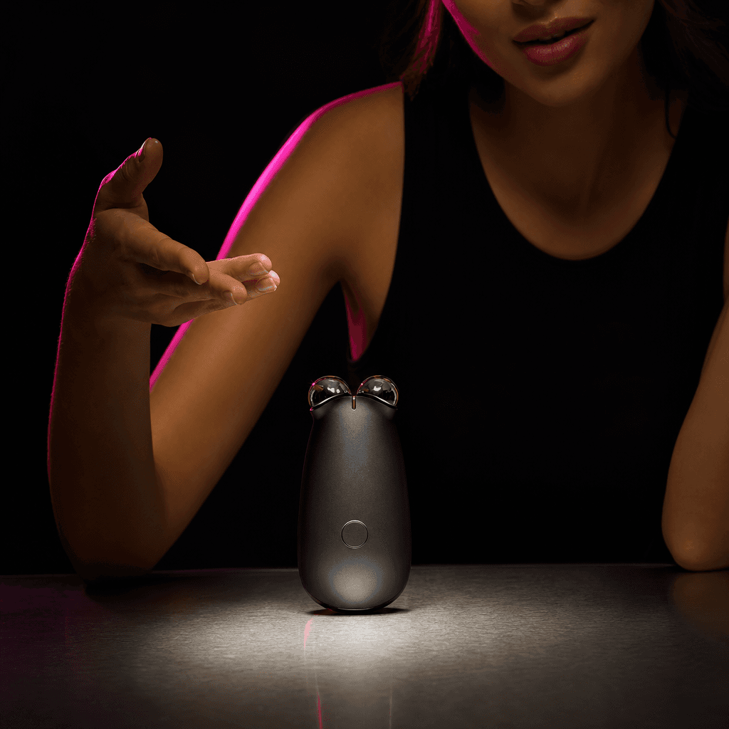 A compact electronic beauty device centered on a brushed metal table, an anonymous creator gesturing confidently beside 