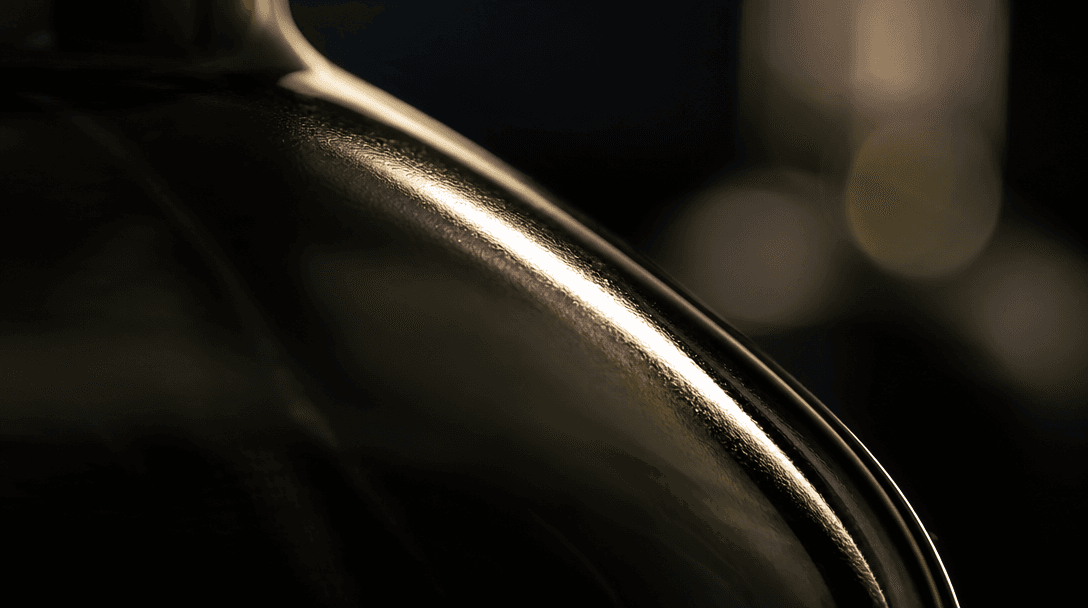 Extreme macro of a dark glass bottle surface catching dramatic sidelight: razor-sharp specular highlight streak, shallow