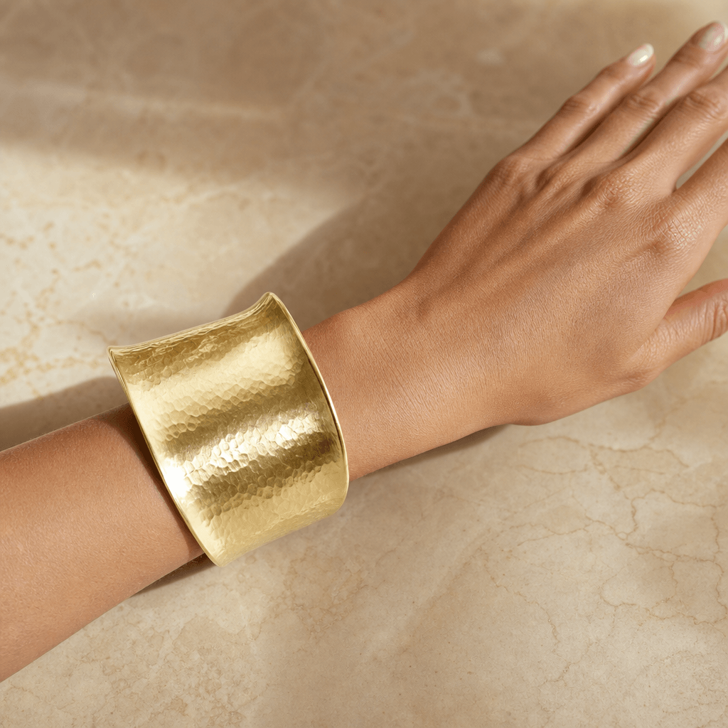 Photorealistic jewelry try-on: a wide hammered gold cuff bracelet on a model's wrist resting against a warm marble surfa
