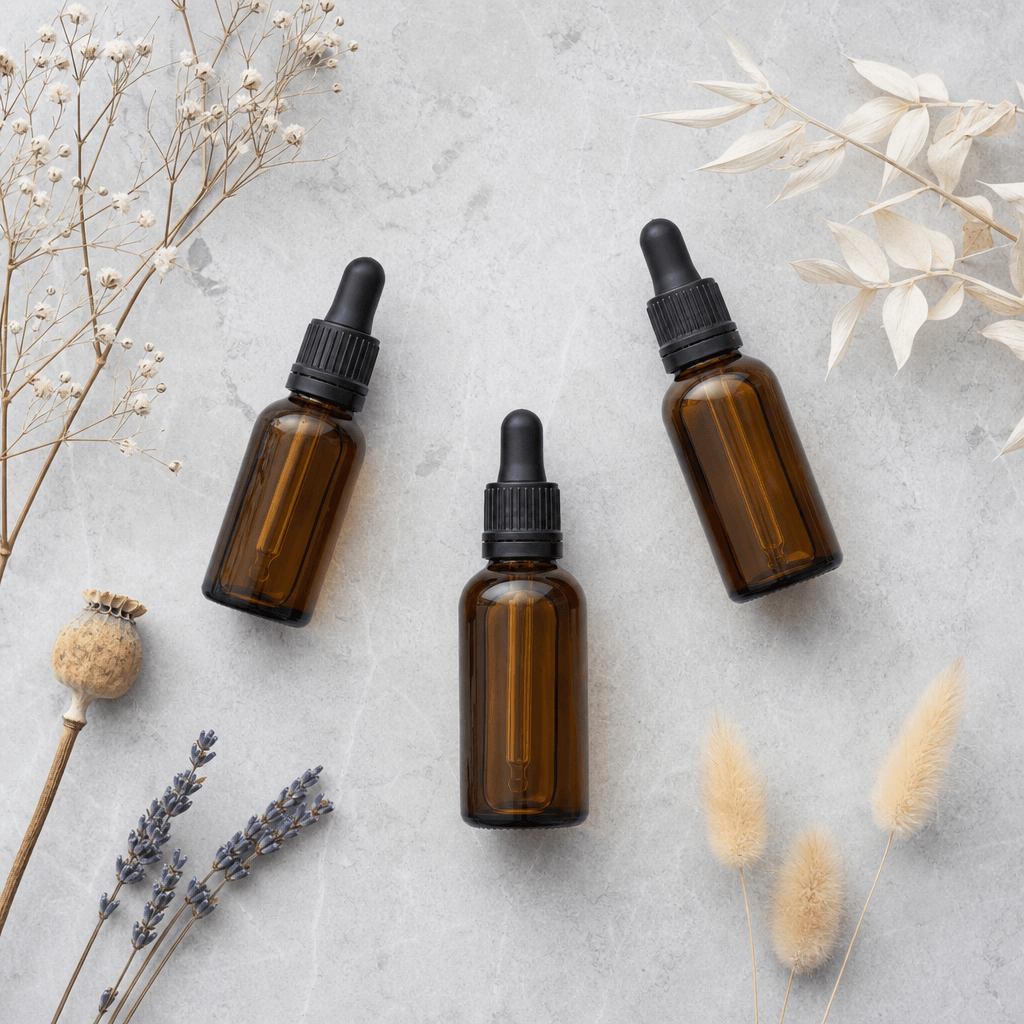 Skincare flat lay on a cool grey stone surface: three minimalist amber glass dropper bottles arranged in a triangle, sur