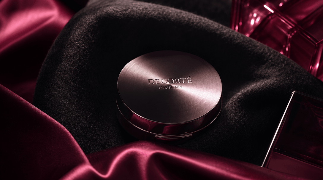 Layers of black wool, burgundy satin, brushed metal, and translucent cosmetic glass forming an atmospheric product stage