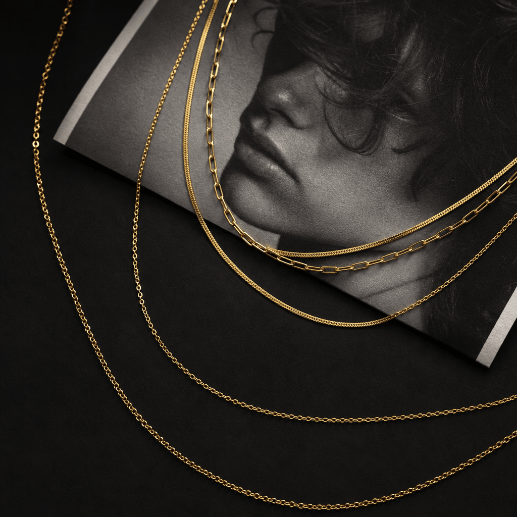 A layered fine gold chain necklace draped loosely across a folded black-and-white photographic print with visible grain 