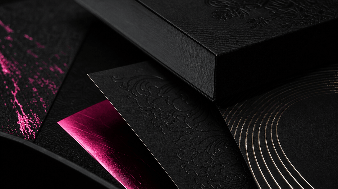 Close-up editorial study of premium bookmaking materials: textured paper, embossed cloth, black ink, metallic foil, and 