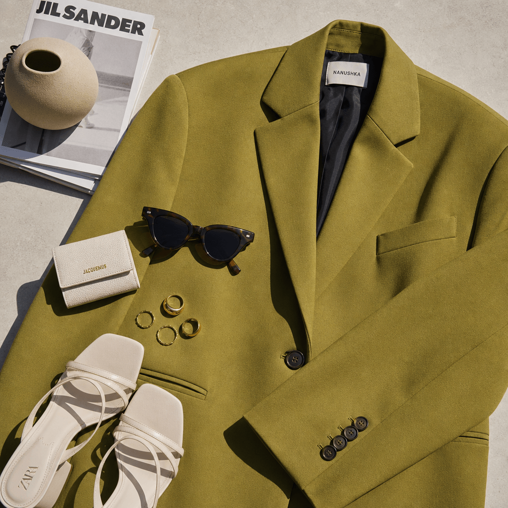 Overhead fashion flat-lay with trendy clothing items—oversized blazer, rings, sunglasses. Editorial lighting, bold color