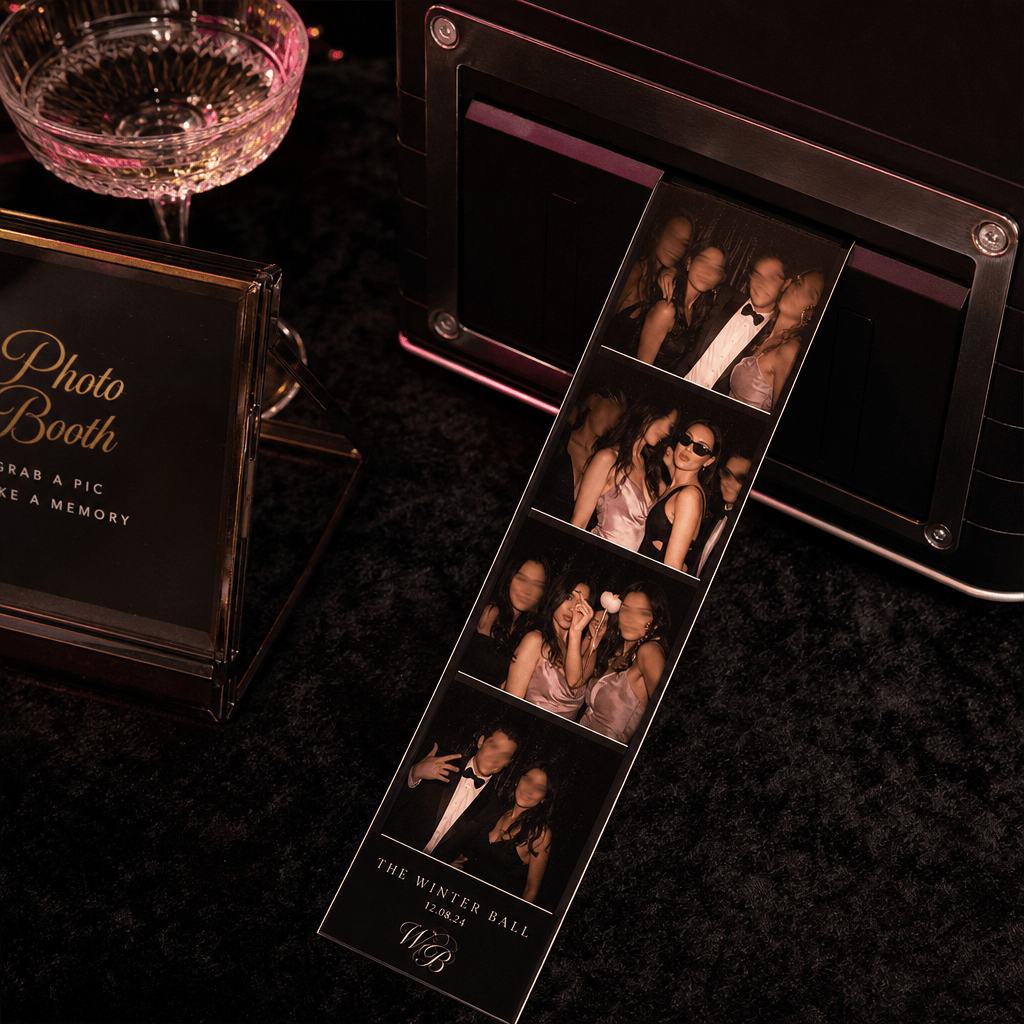 A square luxury event scene with freshly printed photobooth strips emerging onto a dark velvet table, each frame showing