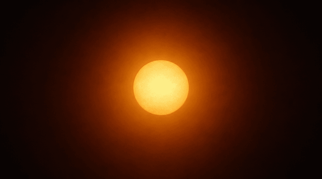 Abstract editorial photograph of a warm luminous sphere of golden-amber light against a deep dark gradient background, s