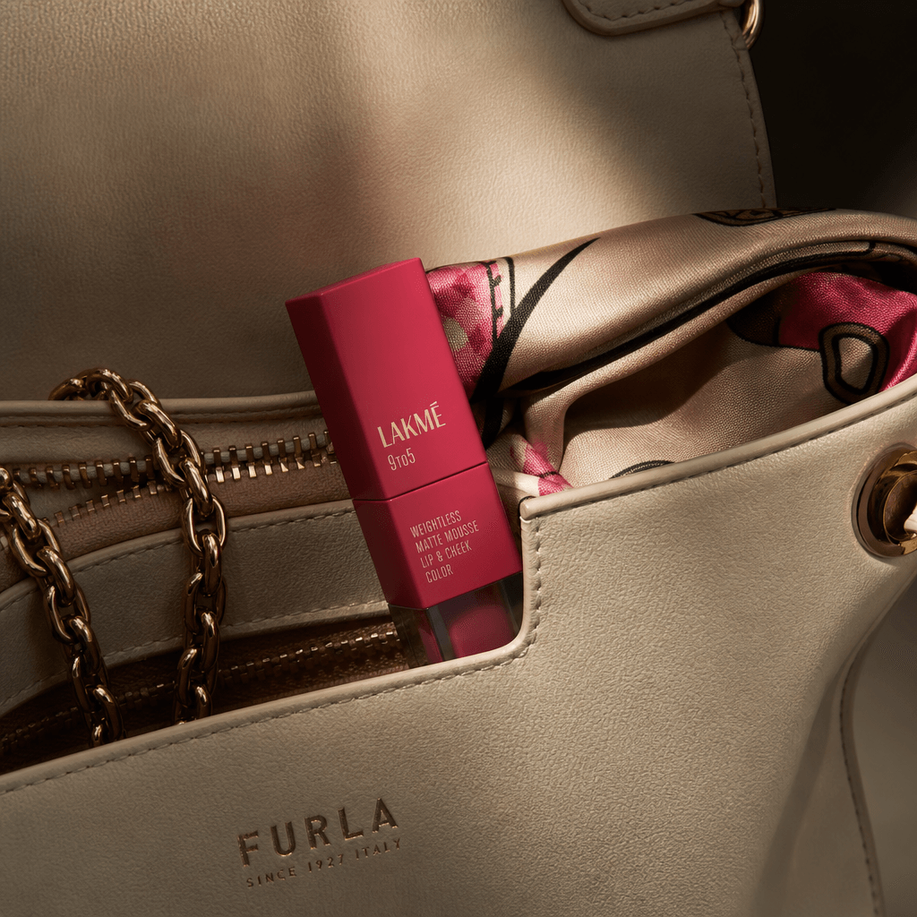 A compact matte lipstick resting inside the pocket of a cream leather handbag, partially revealed beside a fine chain an