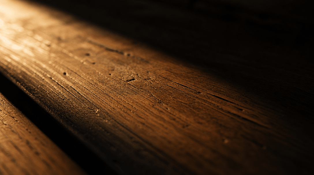 Abstract close-up study of a wooden bench surface lit by a single raking light source, deep shadow on one side, warm amb