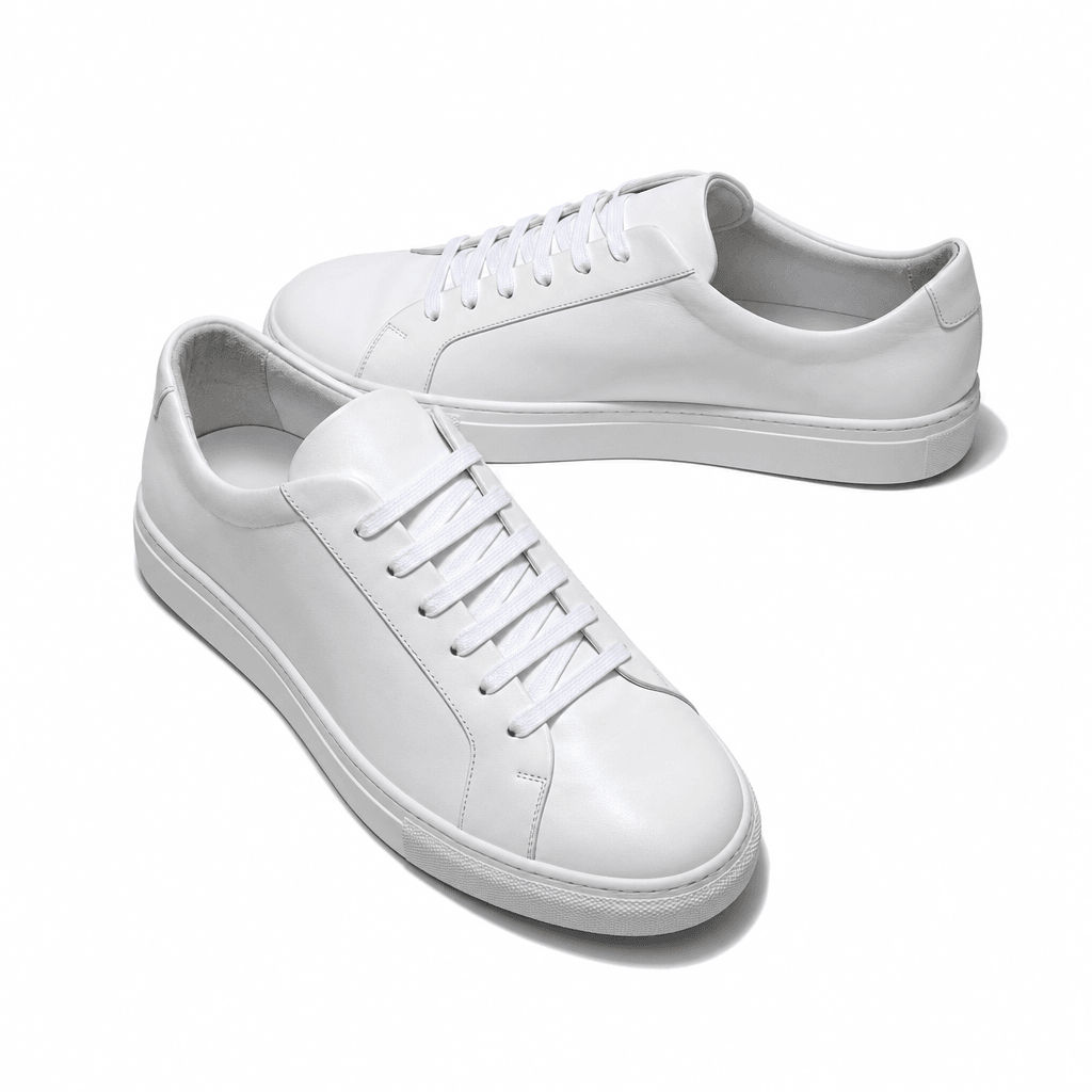 A pair of minimalist white leather sneakers shot on a seamless pure white studio surface, overhead editorial lighting, s