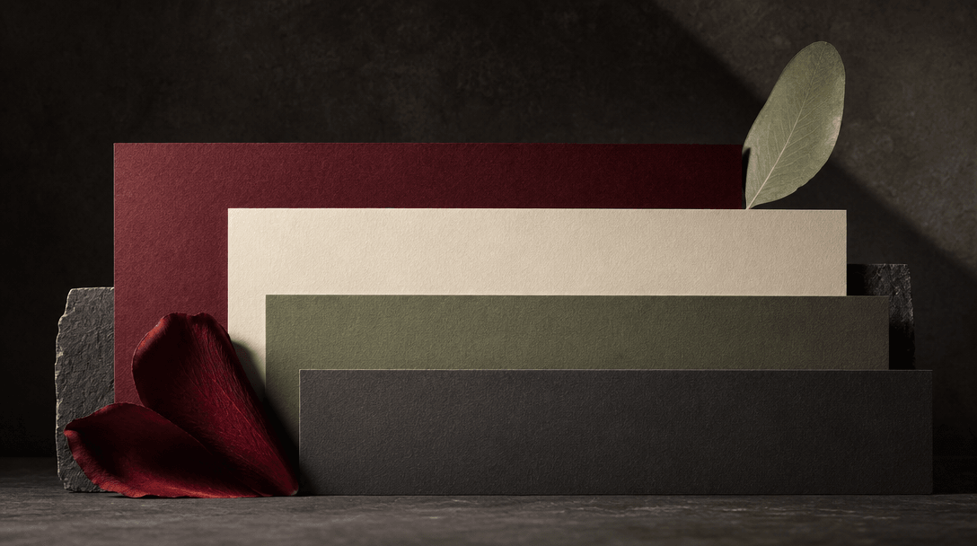 An abstract still life of stacked matte color cards derived from deep red petals, pale cream paper, sage leaves, and cha