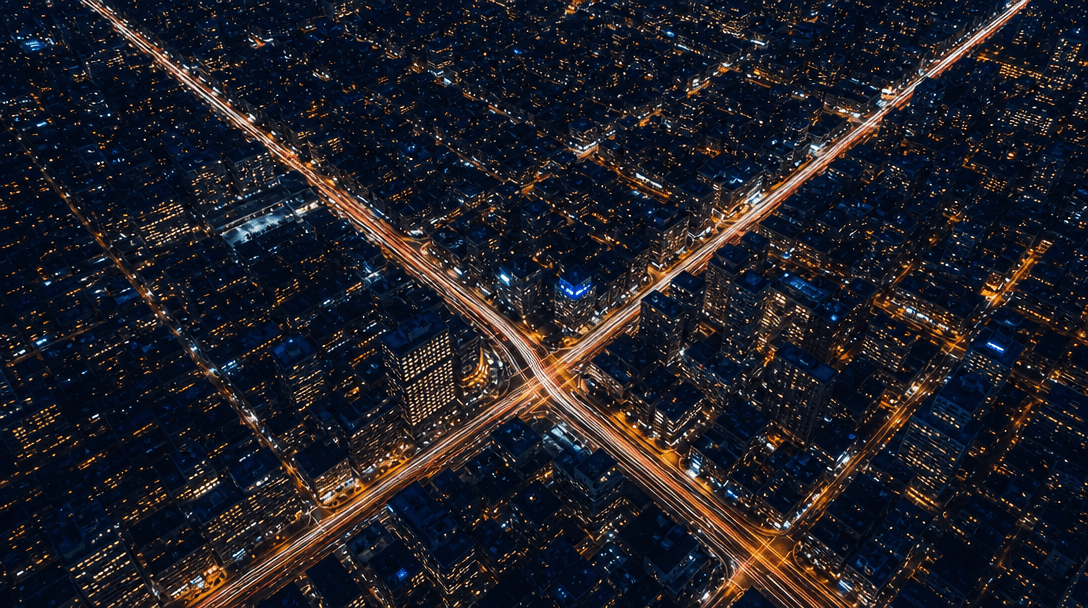 Abstract overhead aerial view of an illuminated city grid at night. Streams of vehicle light trails trace diagonal stree