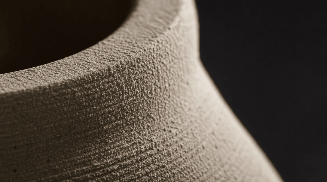 Extreme macro close-up: the unglazed surface of a raw ceramic piece — fine granular ridges and subtle pits catching raki