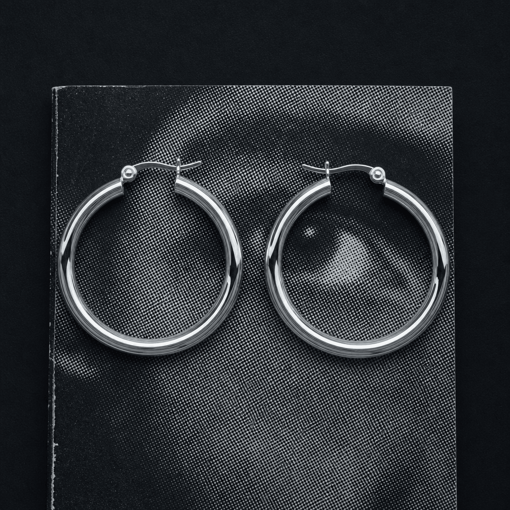 A pair of large silver hoop earrings arranged symmetrically on a textured black-and-white print with visible halftone do
