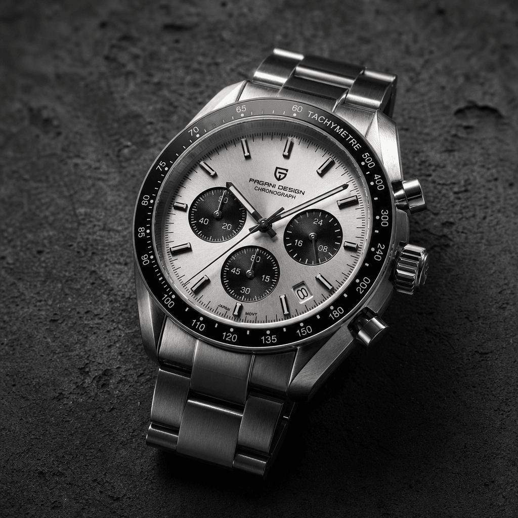 Square editorial product shot: a sleek silver chronograph watch placed on dark textured concrete. Side-lit to emphasise 