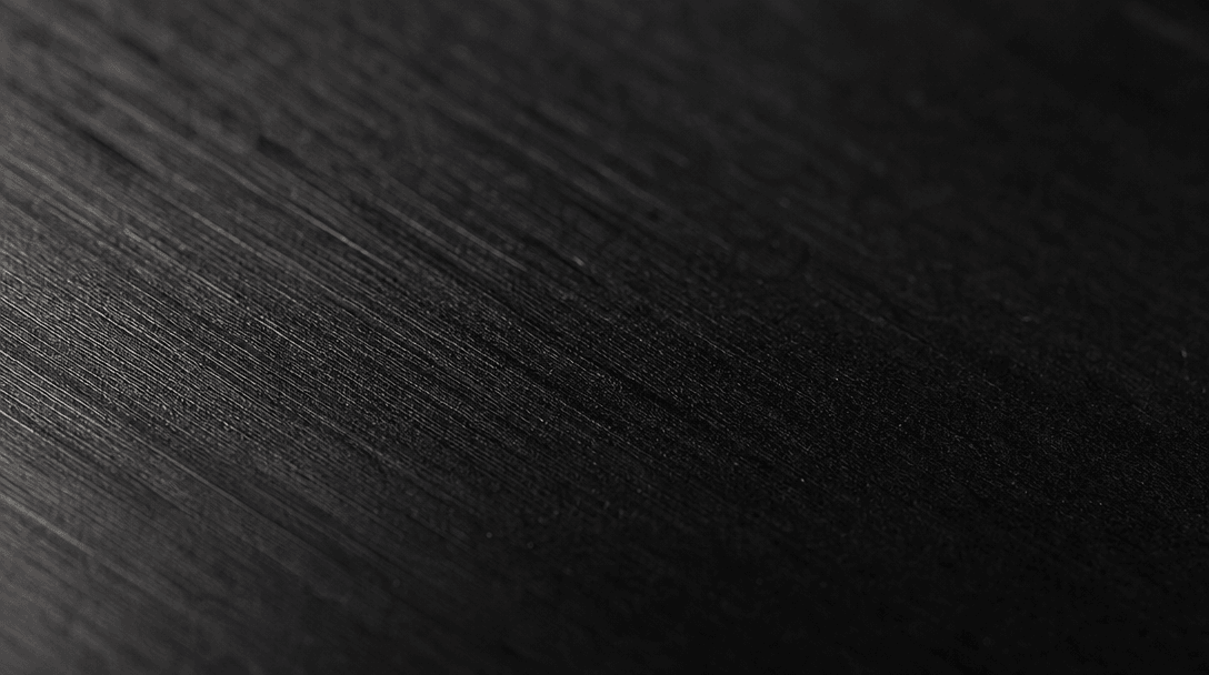Extreme close-up macro of a premium textured material surface — brushed dark metal or matte ceramic — under precision st