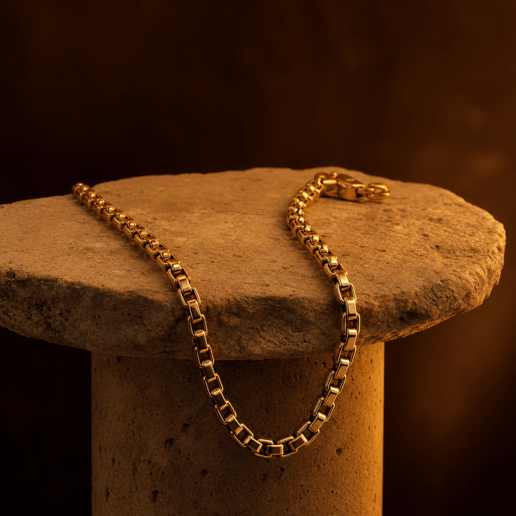 Gold chain necklace draped on stone pedestal with warm amber studio lighting, dark moody background, professional jewelr