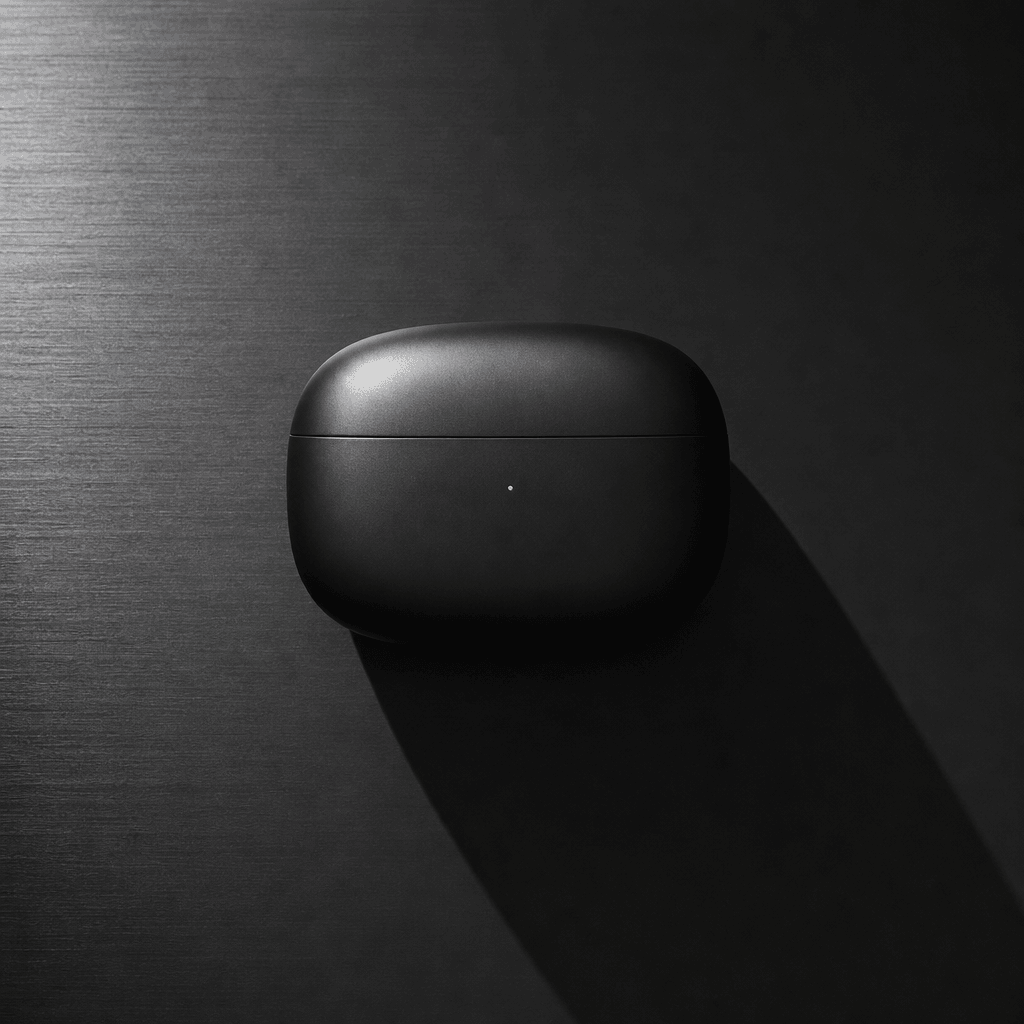A sleek wireless earbud case photographed flat-lay on brushed anthracite surface. Single overhead key light creates hard