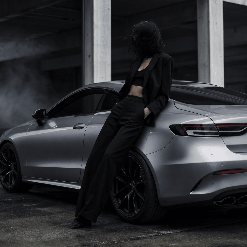 Anonymous fashion model leaning confidently against a silver sports coupe inside a brutalist concrete parking structure,