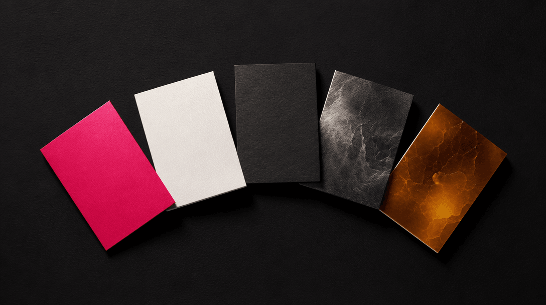 Abstract overhead view of five small sample cards arranged in an arc on a deep matte black surface — each card a differe