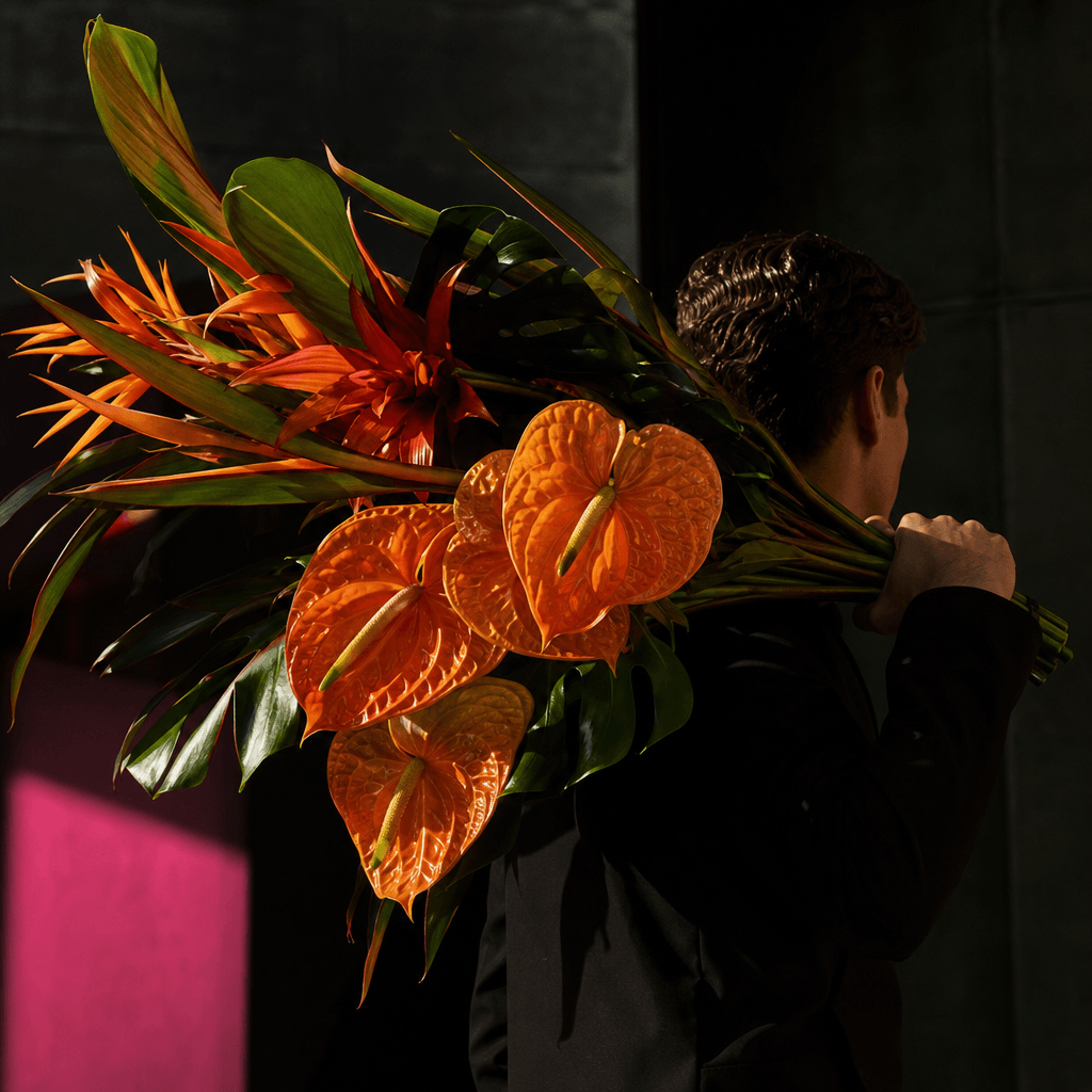 A bold contemporary bouquet of orange anthuriums and sculptural tropical leaves carried over the shoulder of an anonymou