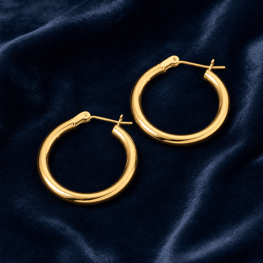 A pair of minimalist gold hoop earrings laid flat on deep navy velvet. Macro-level sharpness, warm studio accent light p