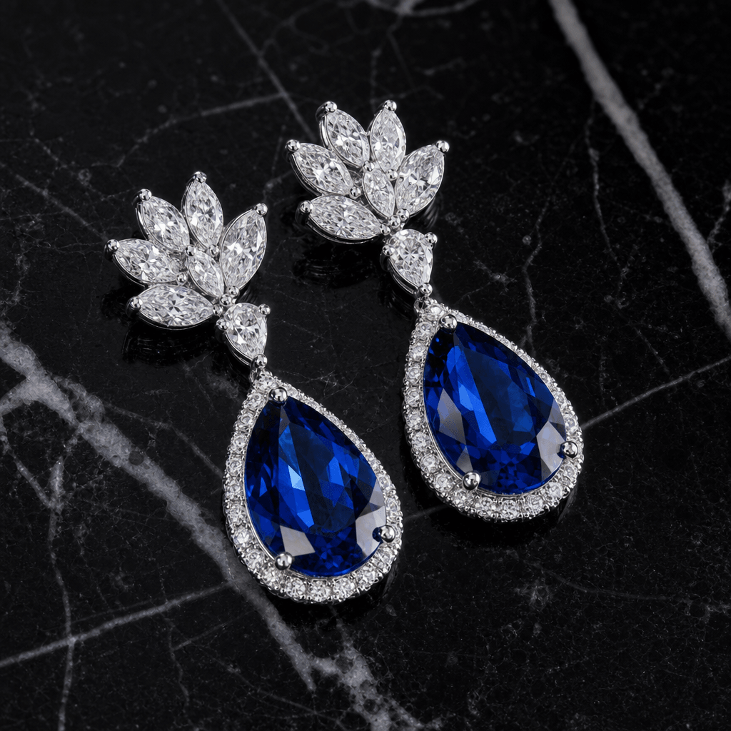Pair of sapphire and diamond drop earrings laid flat on polished black marble, directional side-light creating hard spec
