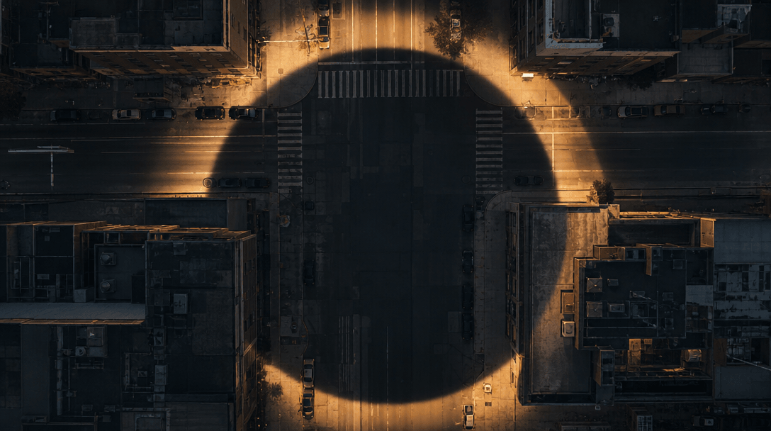 Abstract cinematic overhead aerial shot: a city block at twilight viewed from directly above, a perfect circular shadow 