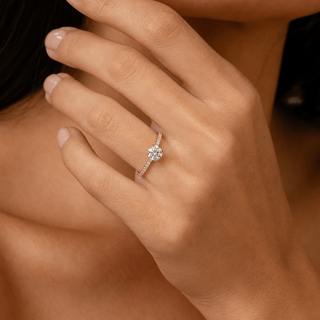 Photorealistic jewelry try-on: a thin gold pavé band ring with a round brilliant diamond solitaire worn on a slender han
