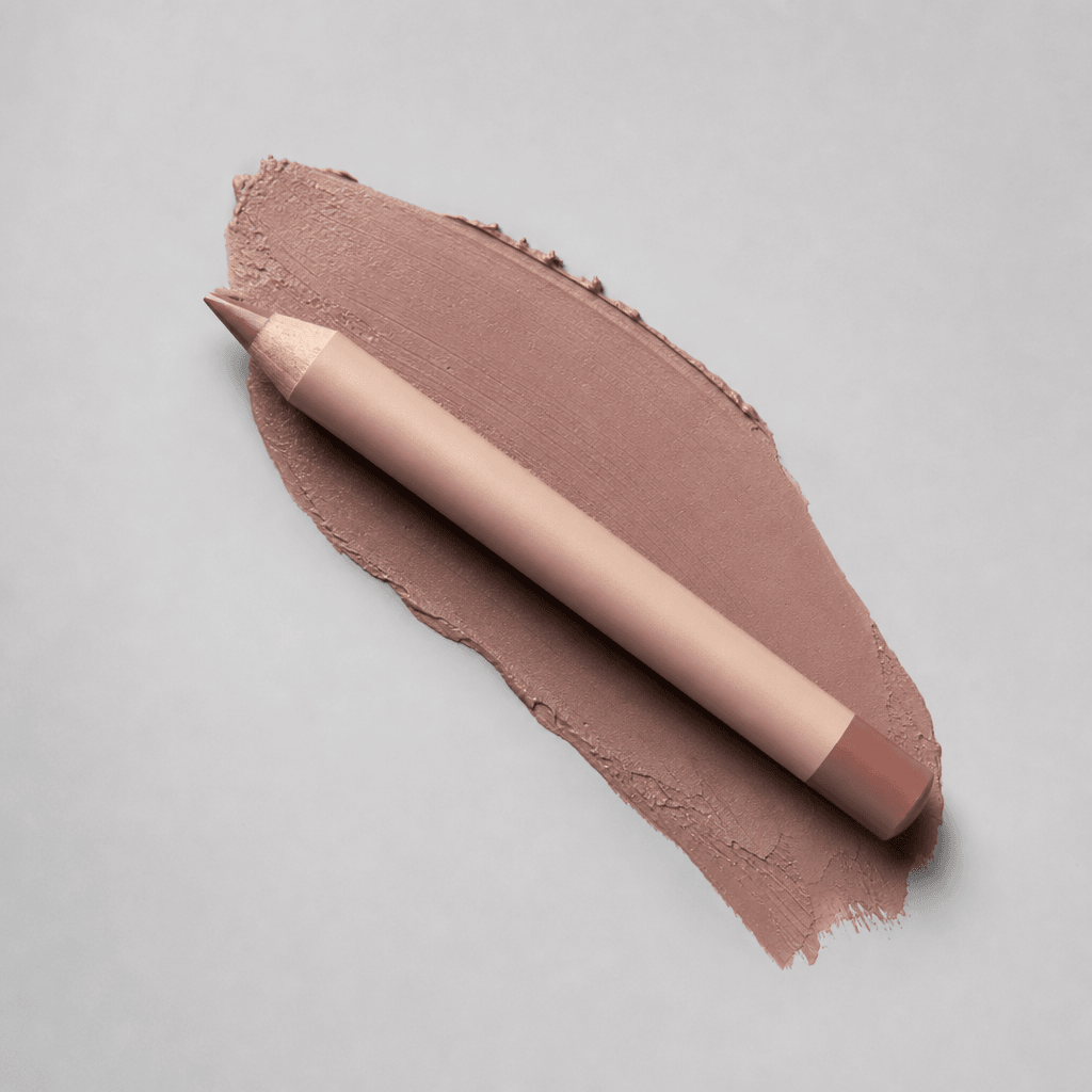 Nude beige lip liner pencil placed at a precise angle over a warm taupe smear on a light grey studio backdrop, diffused 
