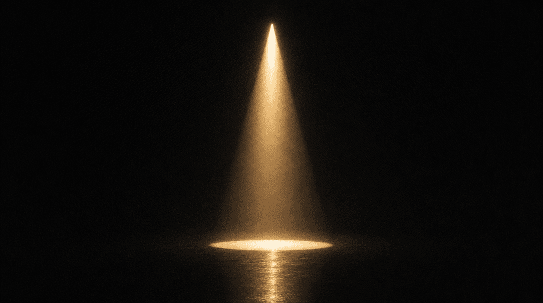 A single tungsten beam of light descends through absolute darkness, casting a sharp perfect cone onto a reflective dark