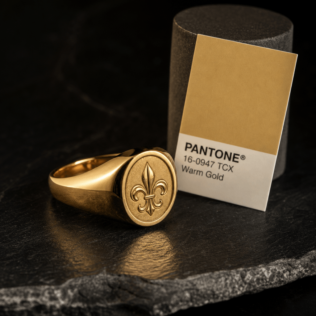 Close-up three-quarter shot of a gold vermeil signet ring resting on a polished dark slate surface. A Pantone Warm Gold