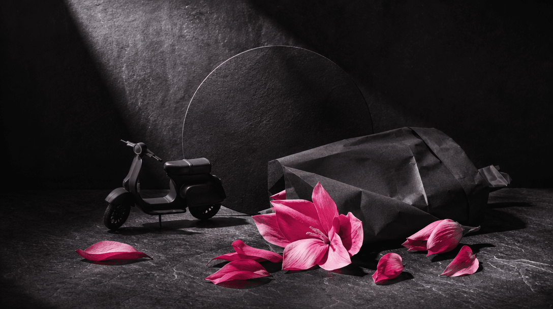 An art-directed still life combining a miniature matte scooter silhouette, fresh flower petals, folded delivery paper, a