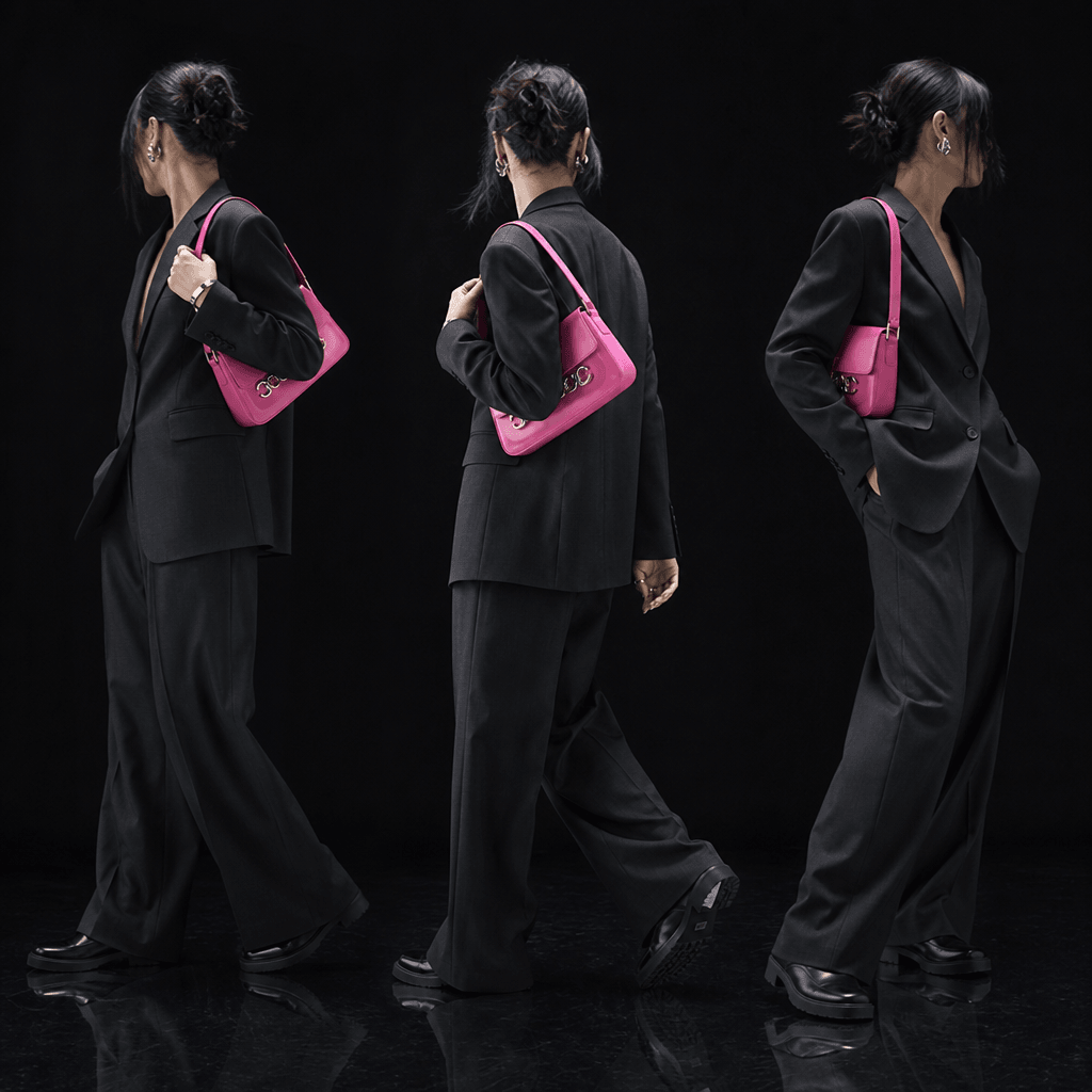 Bold accessories-led try-on image of an anonymous model rotating in a tailored dark suit with a vivid pink bag and silve