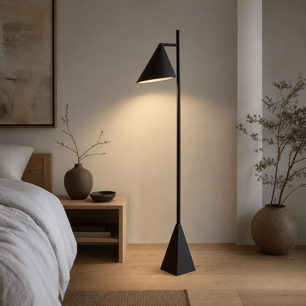 A matte black geometric floor lamp standing in a Japandi-style bedroom. Pale oak hardwood floor, white linen bedding bar